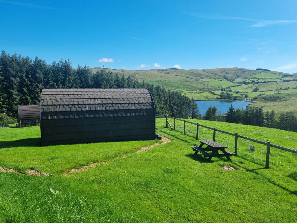 un banco en un campo junto a una valla y un lago en Forester's Retreat Glamping - Cambrian Mountains View en Aberystwyth