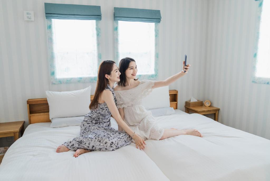 Due donne sedute su un letto con un cellulare in mano di Ecot Irabu Bridge Sunset Hills a Miyakojima