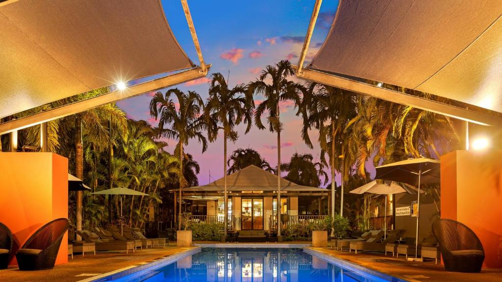 a swimming pool with a building and palm trees at The Pearle of Cable Beach in Broome