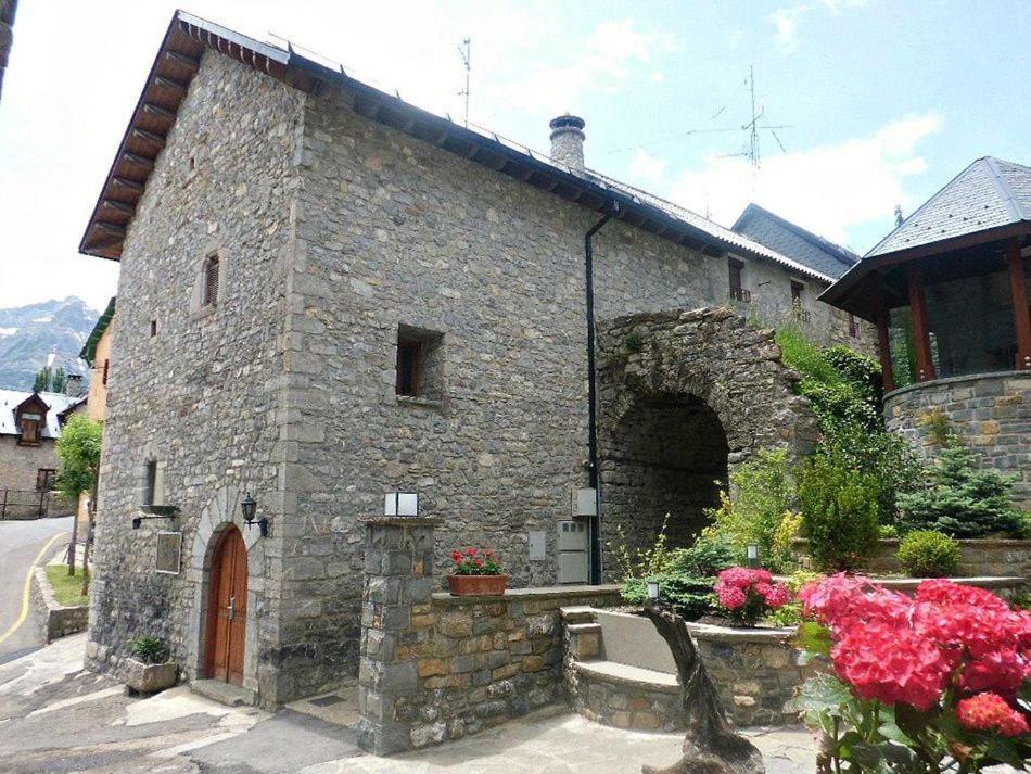 un antiguo edificio de piedra con una puerta y flores en Abadia del Pirineo, en Tramacastilla de Tena