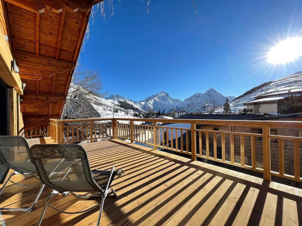 a deck with two chairs on it with snow covered mountains at Odalys Chalet Le Chabichou in Les Deux Alpes