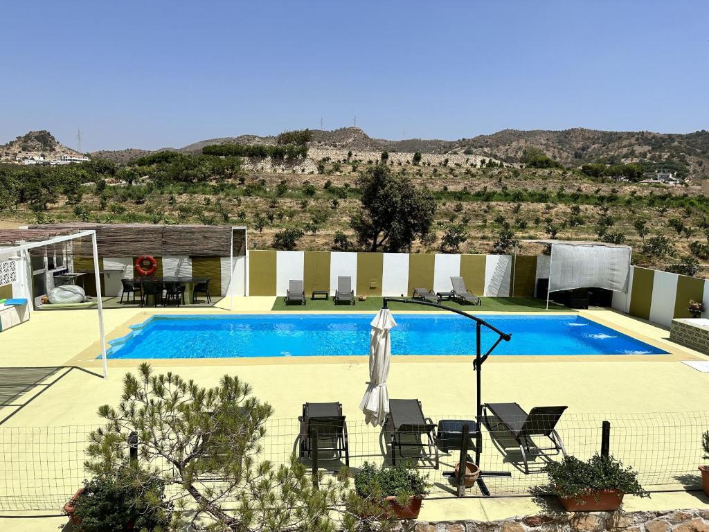a swimming pool with chairs and an umbrella next to it at Casa Rural Humberto con 3 dormitorios in Málaga