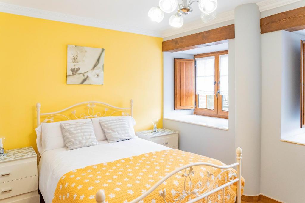 a yellow bedroom with a bed and two windows at La Casita Verde de Cabárceno in Sobarzo