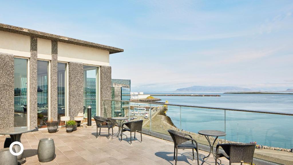 eine Terrasse mit Tischen und Stühlen und Blick auf das Wasser in der Unterkunft Center Hotels Arnarhvoll in Reykjavík