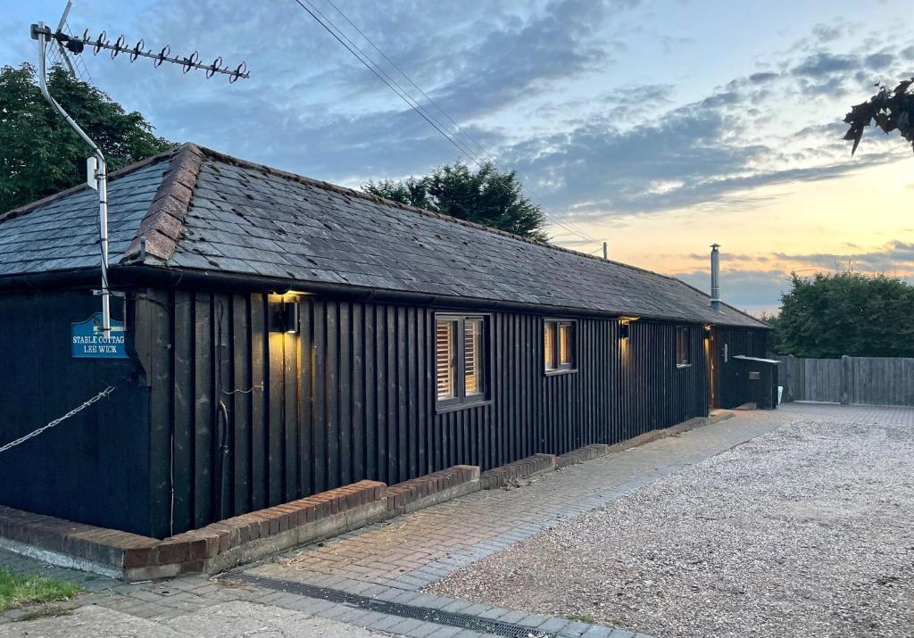 濱海克拉克頓的住宿－Stable Cottage at Lee Wick Farm Cottages & Glamping，一座黑色的建筑,旁边有一个标志