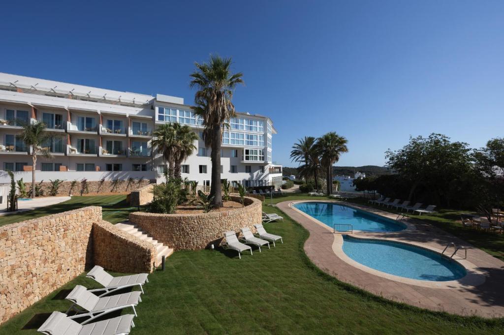 a resort with a pool and lounge chairs and a building at Catalonia Mirador des Port in Mahón