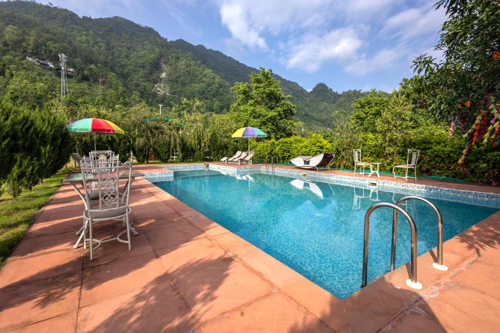 a swimming pool with chairs and umbrellas next to a mountain at Neer Ganga Resorts in Rishīkesh
