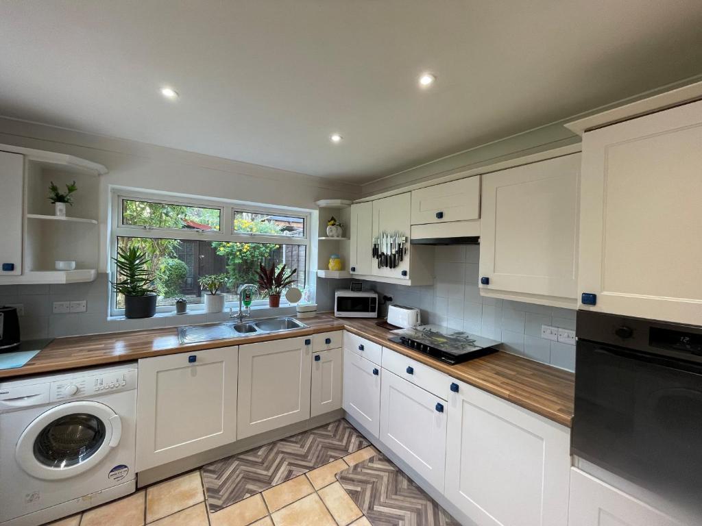 een keuken met witte kasten en een wasmachine en droger bij Addlestone Tranquil Spacious Three Bedroom Bungalow in Addlestone