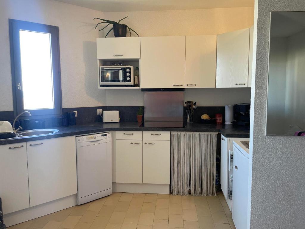 a kitchen with white cabinets and a microwave at La pénate de Saint Cyp - résidence les Frégates vue mer, Piscine in Saint-Cyprien