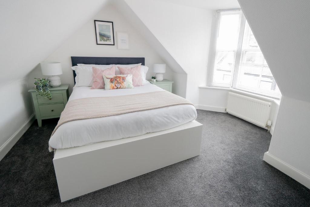 a white bedroom with a large bed with pink pillows at Coorie by the Coast - Arbroath in Arbroath