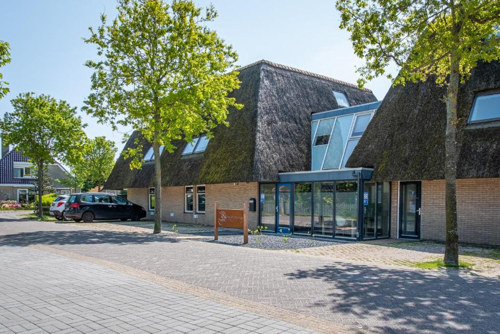 a building with a grass roof with a parking lot at Waddenresidentie Ameland Zilt, een ruim 4-persoons appartement in Buren
