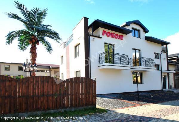 a white building with a fence and a palm tree at Pokoje Gościnne Wejherowo in Wejherowo