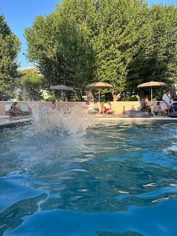 a pool of water with people sitting on chairs and umbrellas at Hotel St Gregory Park in Rimini