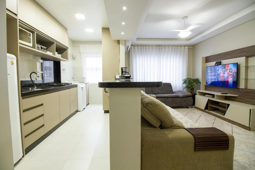 a kitchen and living room with a couch and a tv at Apto Germano Praia in Balneário Camboriú