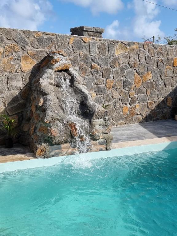 a stone wall and a swimming pool with a waterfall at Eleganz Residence in Grand Baie