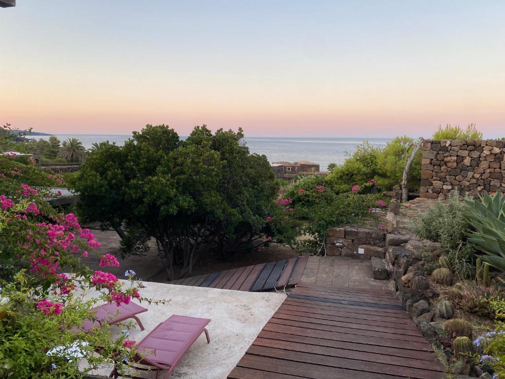 un jardin avec des bancs et des fleurs roses et l'océan dans l'établissement Dammuso Tuffo nel mare, à Pantelleria