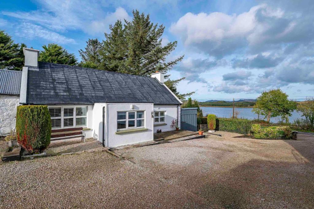 a small white house with a garage next to a lake at Traditional Cottage with Private Hot Tub in the Heart of Donegal in Letterkenny
