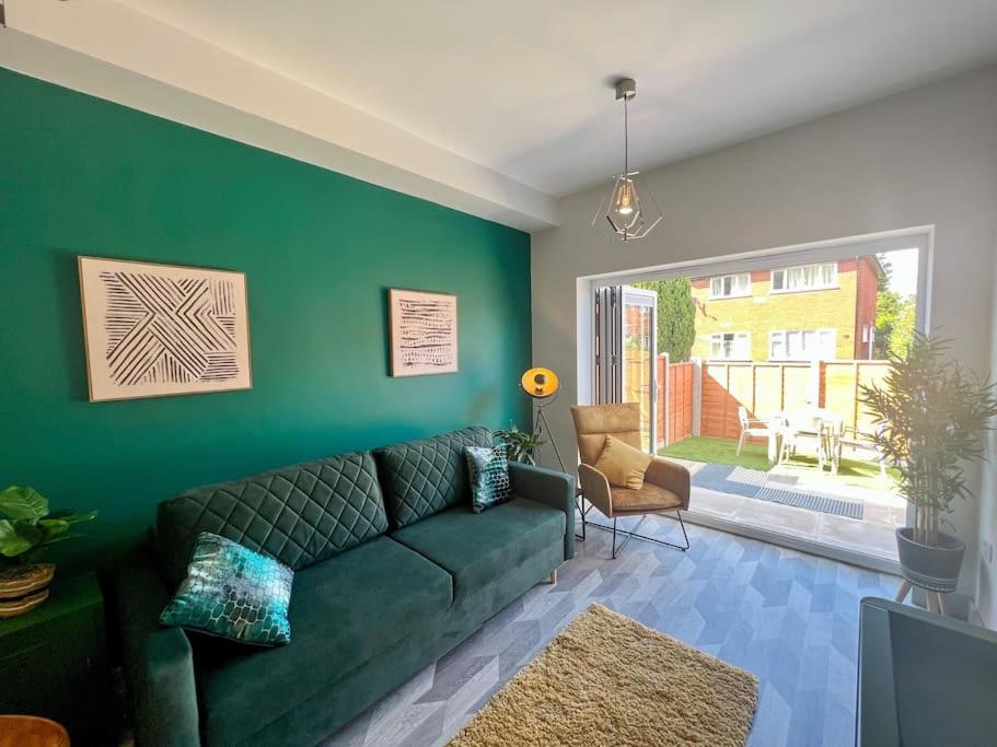 Modern 2 Bed House With EV Parking في Henwick: غرفة معيشة مع أريكة خضراء وجدار أخضر