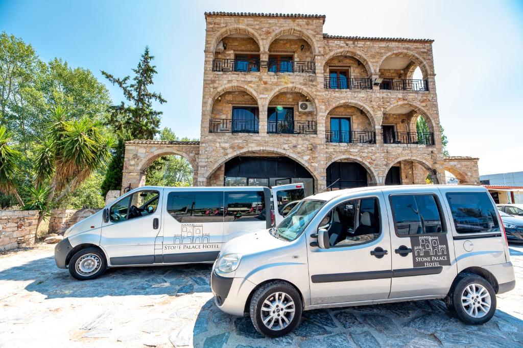 Due furgoni bianchi parcheggiati di fronte a un edificio di Stone Palace Hotel Free Shuttle From and to Athen's Airport a Spata
