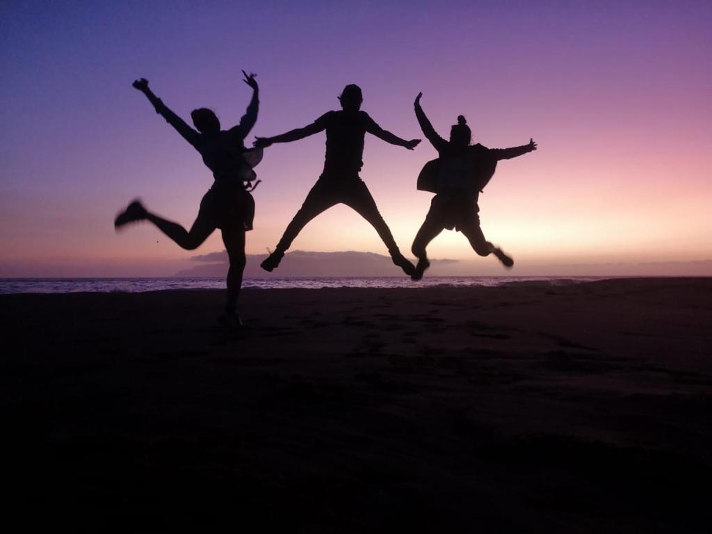 drie mensen springen op het strand bij zonsondergang bij Pensao Zé Doce in Portela