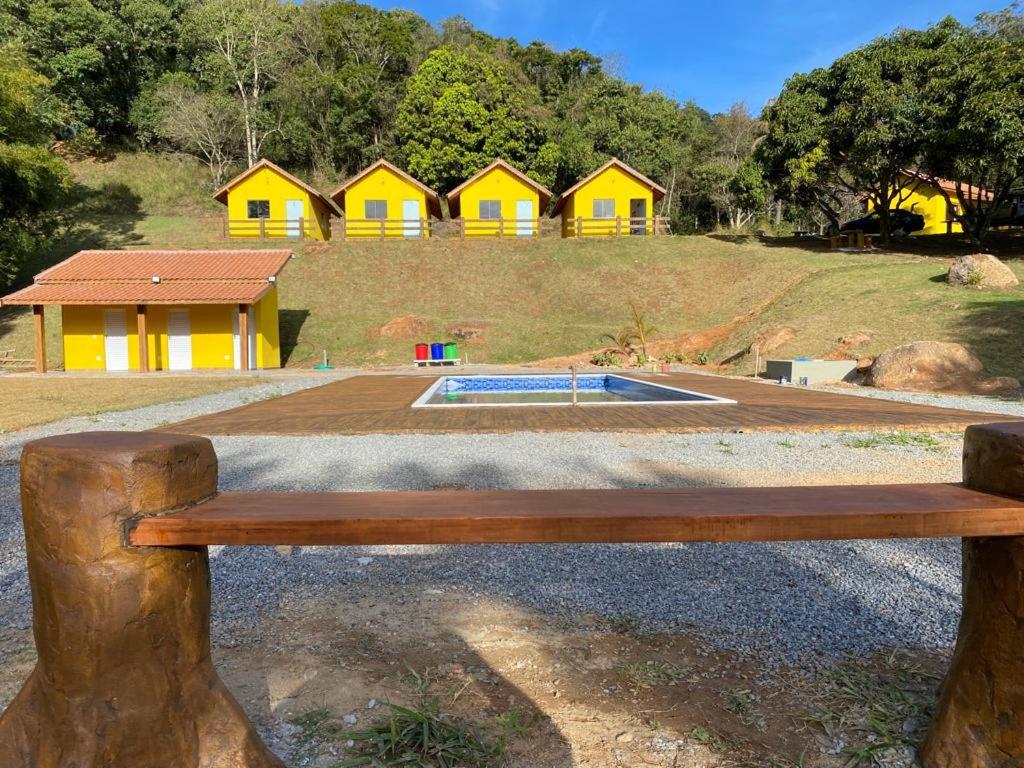 um banco de madeira em frente a um grupo de habitações amarelas em Eco Chalés Pedra Bela em Pedra Bela
