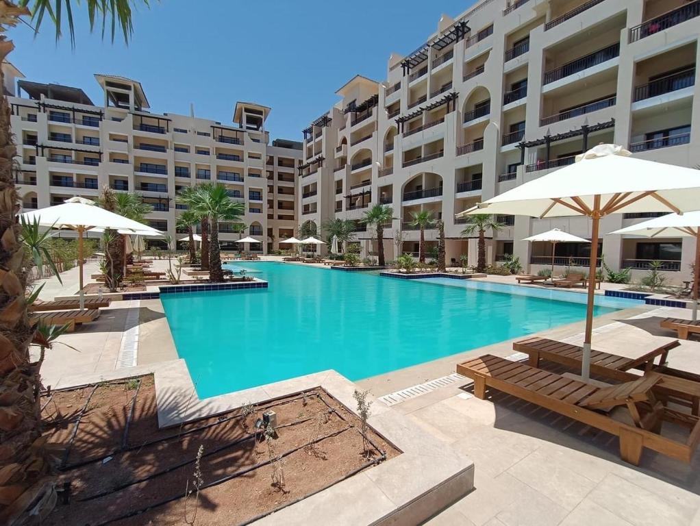 - une piscine avec des bancs et des parasols en face d'un bâtiment dans l'établissement AlDau Heights Apartments, à Hurghada