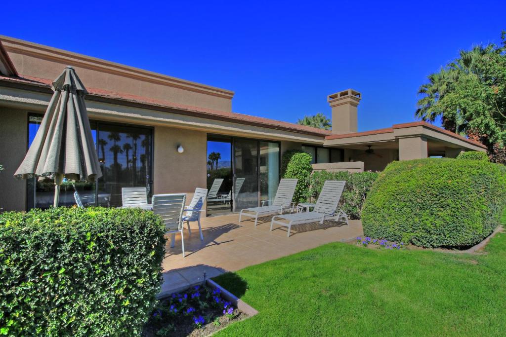 uma casa com um pátio com um guarda-sol e cadeiras em VS555 - Palm Views em Palm Desert