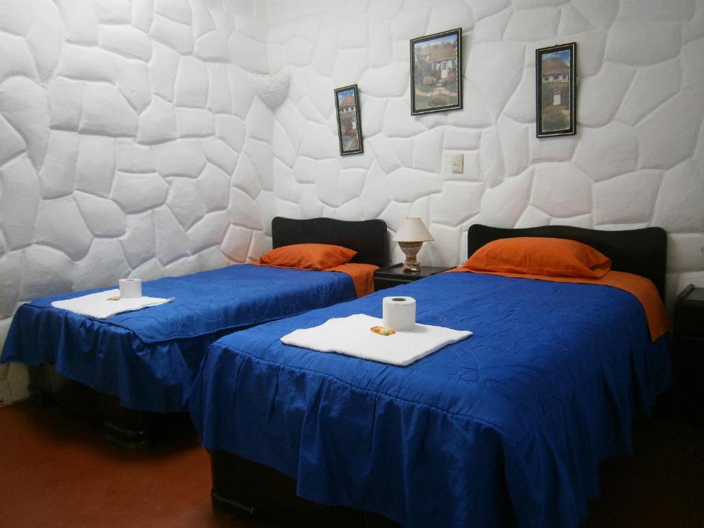 2 camas en una habitación con sábanas azules y almohadas de color naranja en Wulzer Samana Wasi Andahuaylillas, en Andahuaylillas