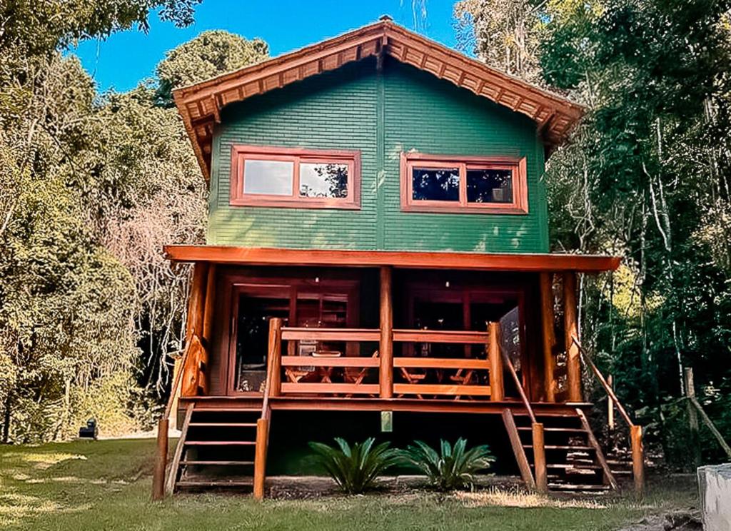 een groen huis met een grote veranda en een trap. bij Chale pe na areia c WIFI -Praia do Peixe Grande BA in Prado