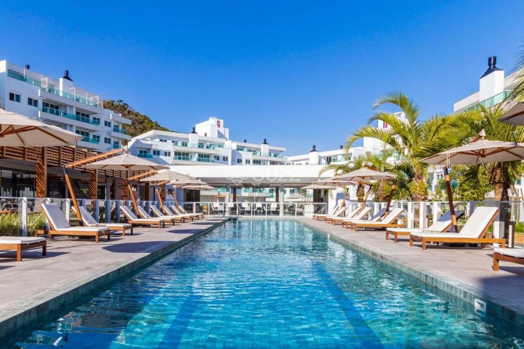 a swimming pool with lounge chairs and umbrellas at a resort at Jurerê Beach Florianópolis ville romane in Florianópolis