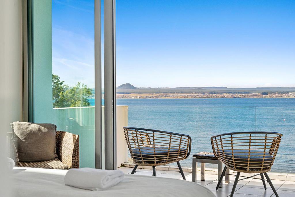 a bedroom with a bed and two chairs and a view of the water at Taupo Penthouse in Taupo