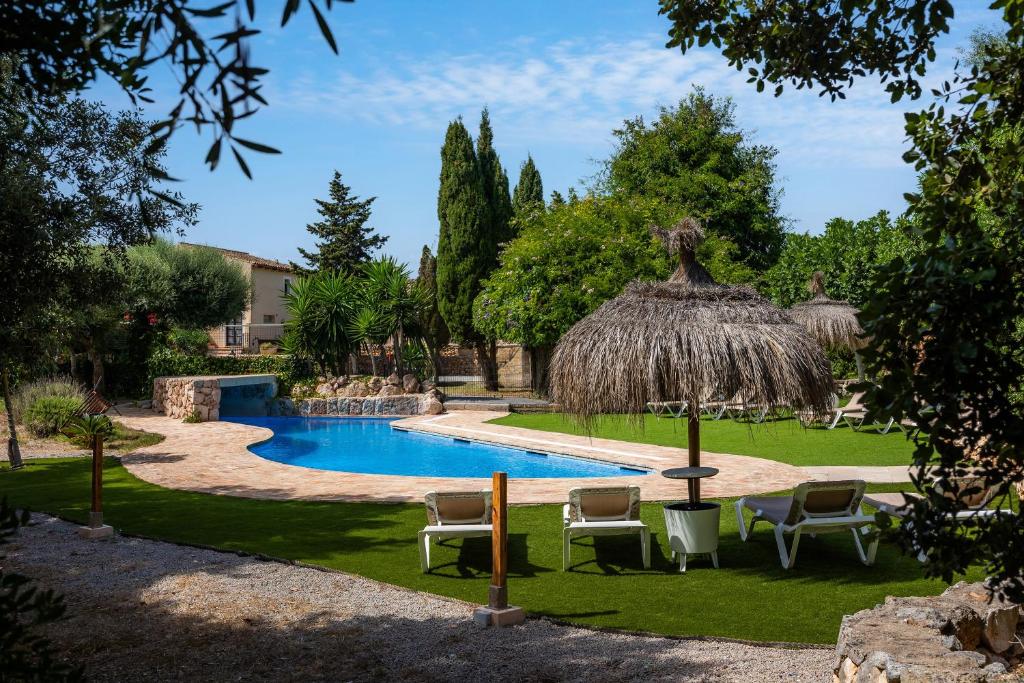 a resort with a swimming pool with chairs and a straw umbrella at Finca Son Favar Capdepera in Capdepera