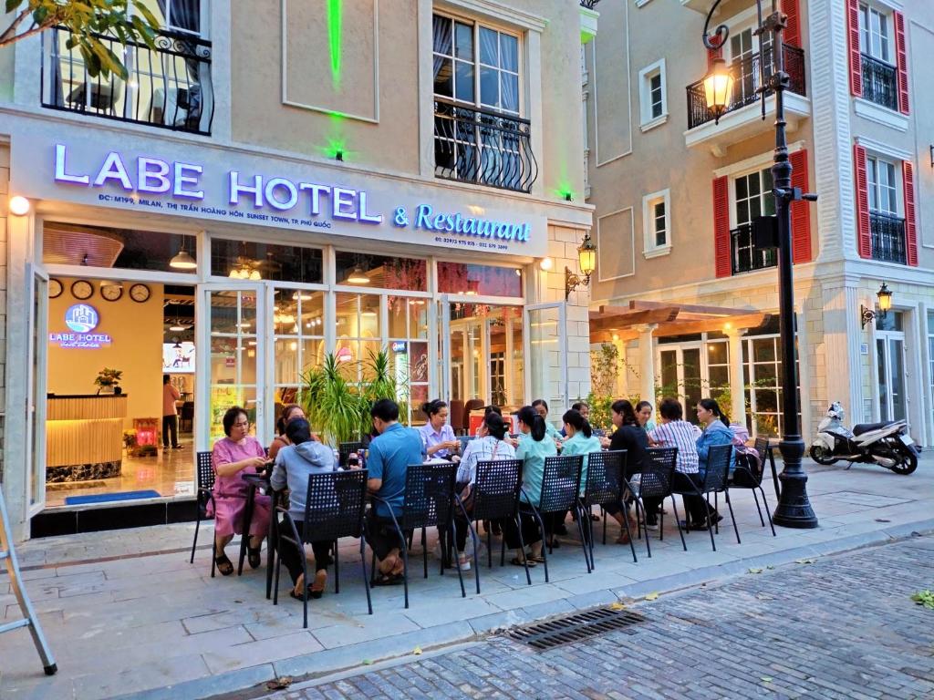Labe Hotel Phú Quốc - Sunset Town - Địa Trung Hải في فو كووك: مجموعة اشخاص جالسين على طاولة امام الفندق