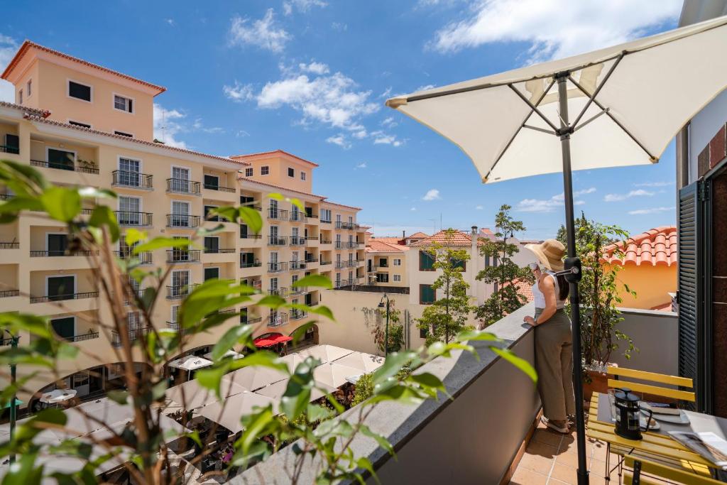 a woman standing on a balcony with an umbrella at Apartamento na Praça by An Island Apart in Funchal