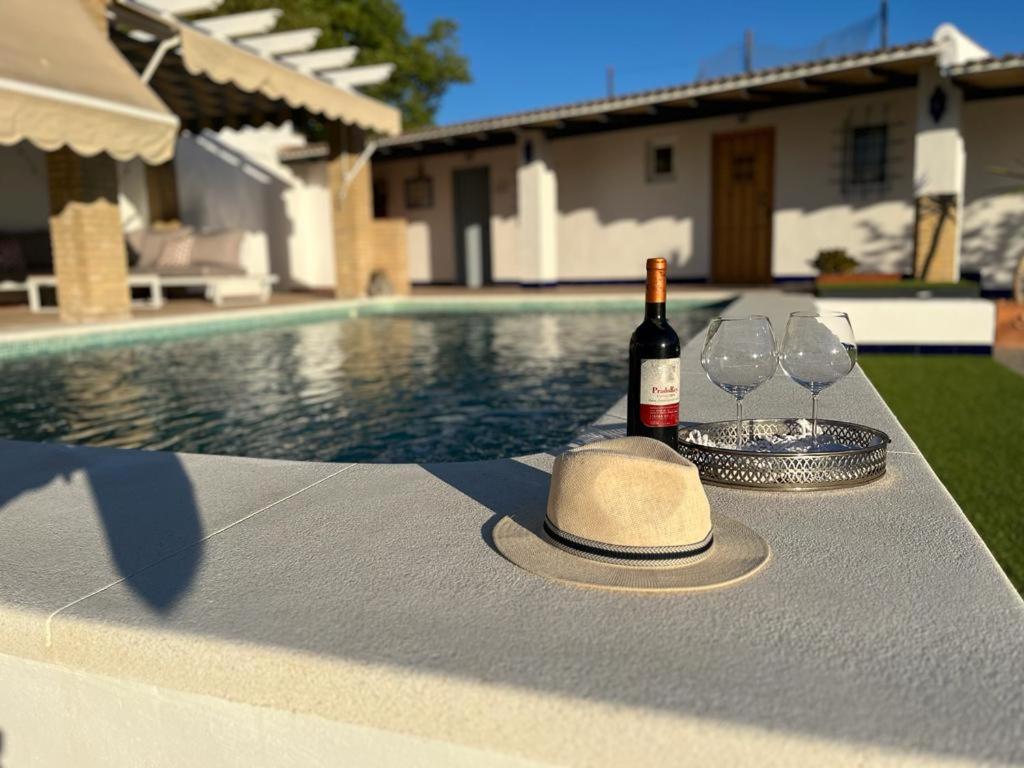 una botella de vino y copas en una mesa junto a la piscina en El Patio de las Minas, en Aznalcázar