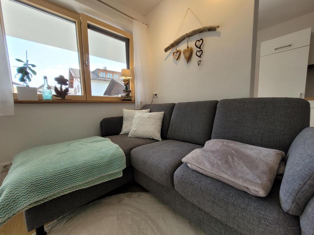 a living room with a gray couch and a window at Ebenerdige Ferienwohnung Beim Schmölz in Hopferau