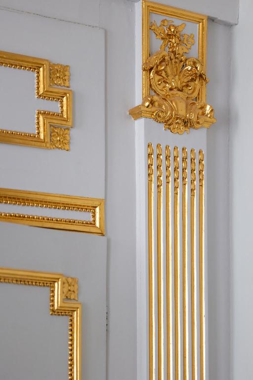 a row of gold frames on a white wall at Hotel Le Place d'Armes - Relais & Châteaux in Luxembourg
