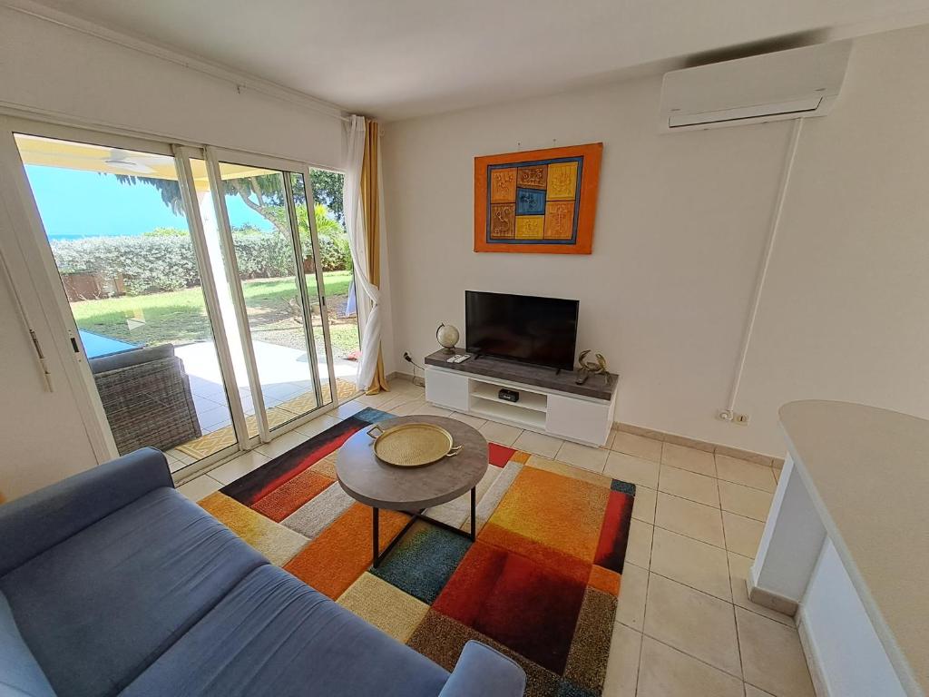 a living room with a couch and a table and a tv at RDC appartement en bord de mer au son des vagues in Le Moule