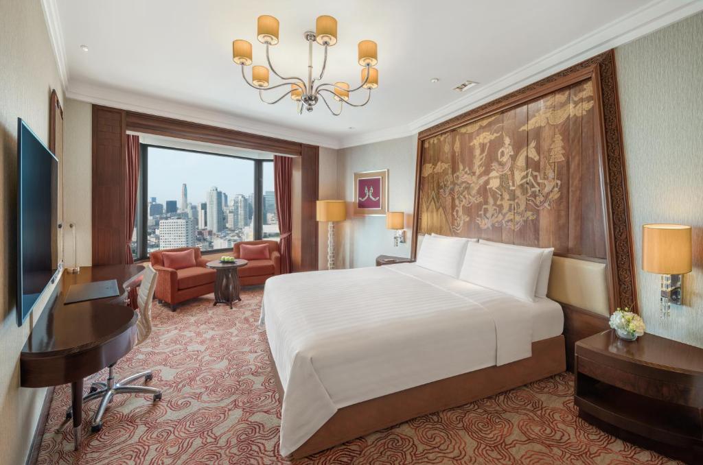 A bright traditional bedroom with a work desk, television, and daytime skyline view.