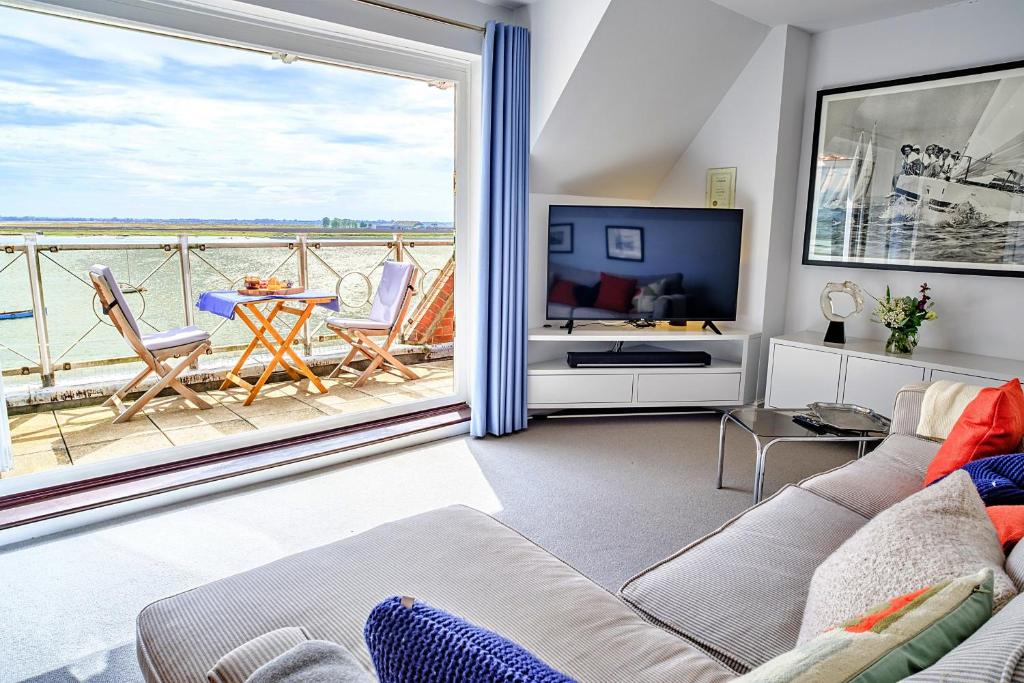 a living room with a couch and a tv and a balcony at Finest Retreats - Kings Wharf - Luxury Riverside Home in Burnham-on-Crouch