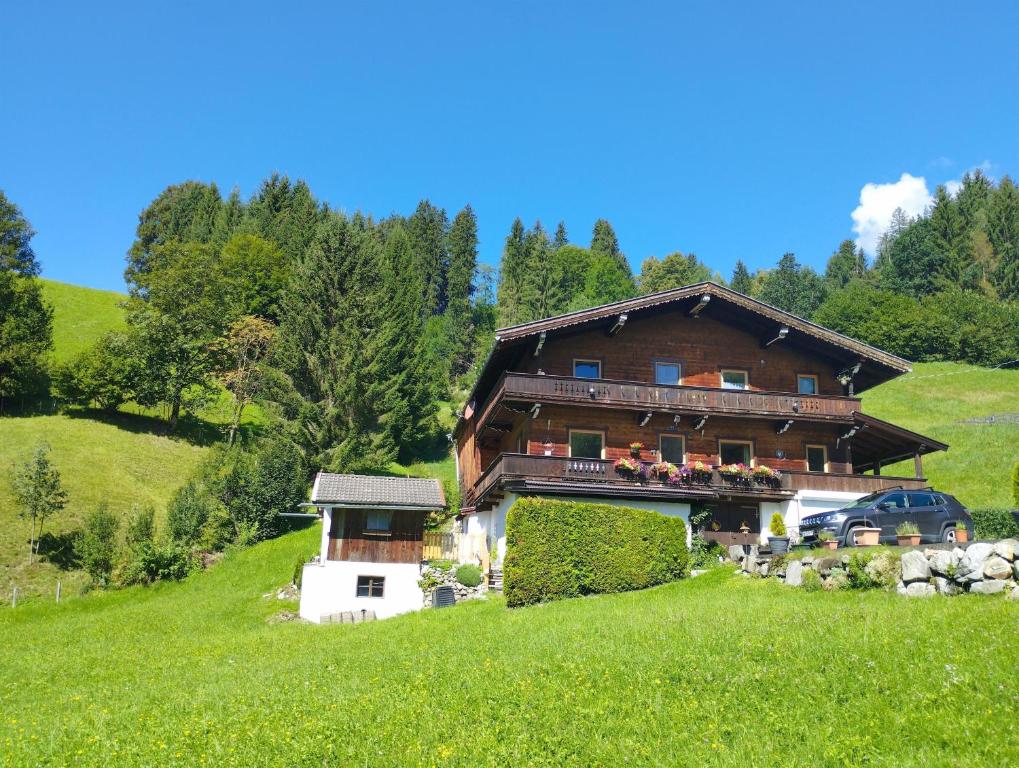 une grande maison en bois sur une colline avec un champ verdoyant dans l'établissement Ferienwohnung Ehrensberger, à Brixen im Thale