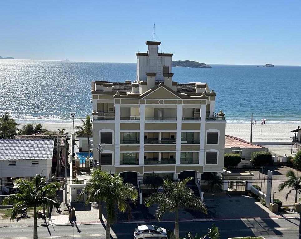 un gran edificio blanco con el océano en el fondo en Golfinhos Apart Hotel, en Florianópolis