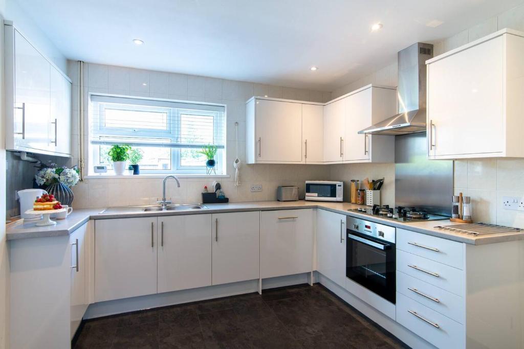 a white kitchen with white cabinets and a sink at Immaculate home close to City Centre with large drive in Derby