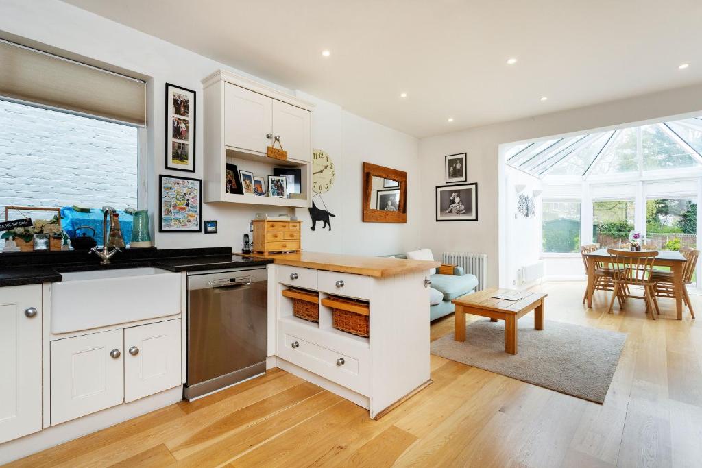 a kitchen with white cabinets and a living room at Veeve - Kew Grass House in Kew