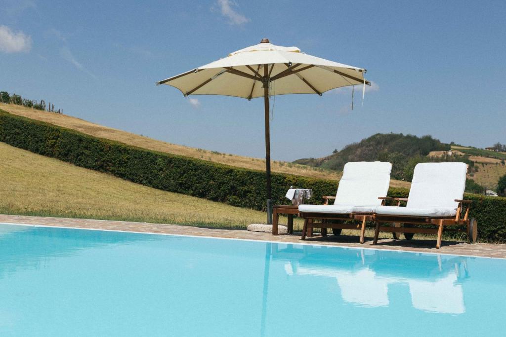 2 sillas y sombrilla junto a la piscina en Apart-Agriturismo "La Colomba" Nizza Monferrato, en Nizza Monferrato