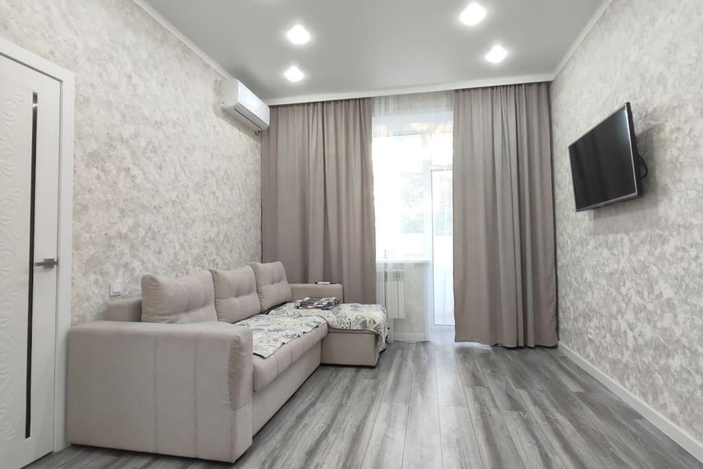 ein Wohnzimmer mit einem weißen Sofa und einem TV in der Unterkunft Люкс апартаменты в ЖК Shanyrak in Pawlodar