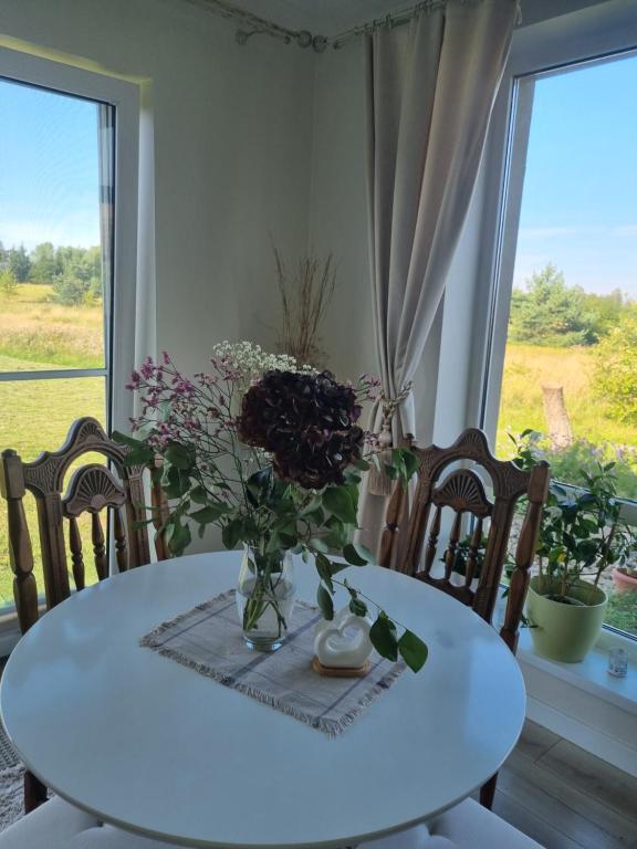 ein weißer Tisch mit einer Vase Blumen drauf in der Unterkunft Vilmos House in Vydmantai