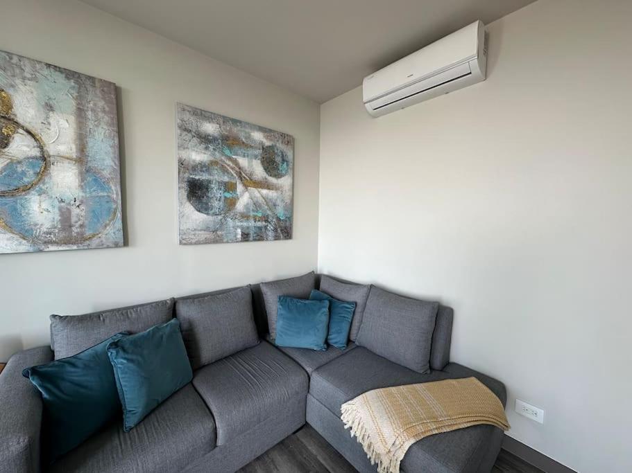 a living room with a gray couch with blue pillows at Panoramic view apt with A/C near SJO Airport & Stadium, Cosmopolitan Tower in San José