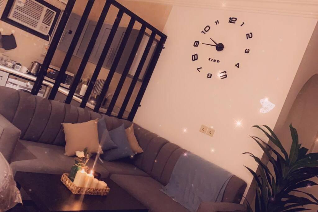 Taibah Apartment في المدينة المنورة: غرفة معيشة مع أريكة وساعة على الحائط