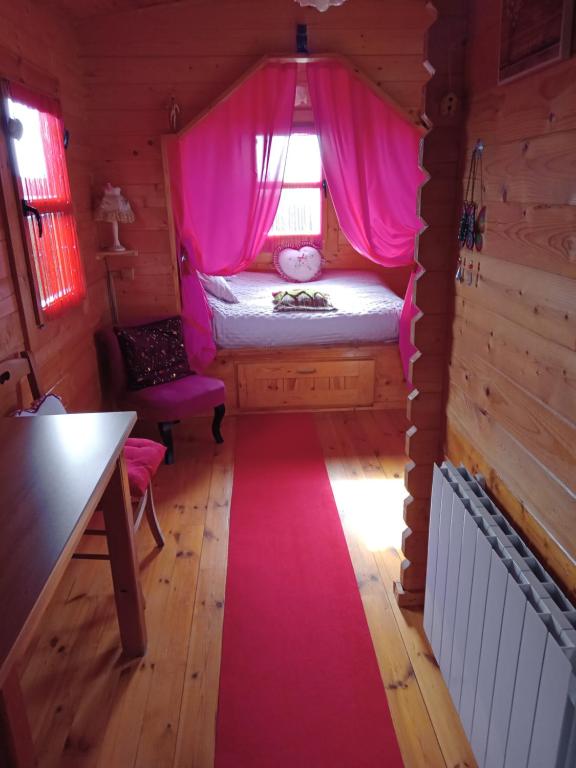 a bedroom with a bed with pink curtains and a red rug at Roulotte la passe pierre in Pendé